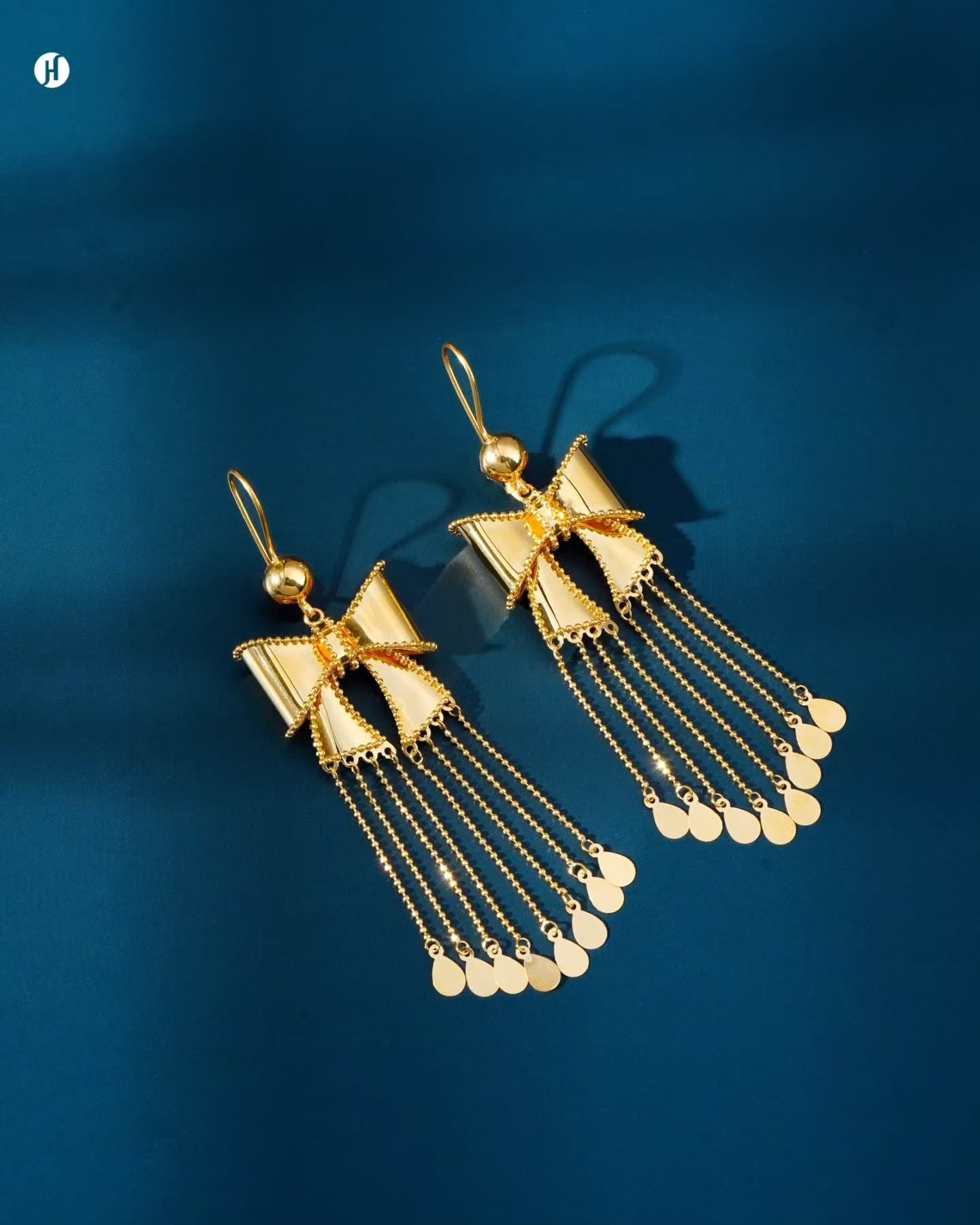 21K yellow gold Bahraini hook earrings with a bow motif and flowing tassel chains tipped with gold teardrop discs.