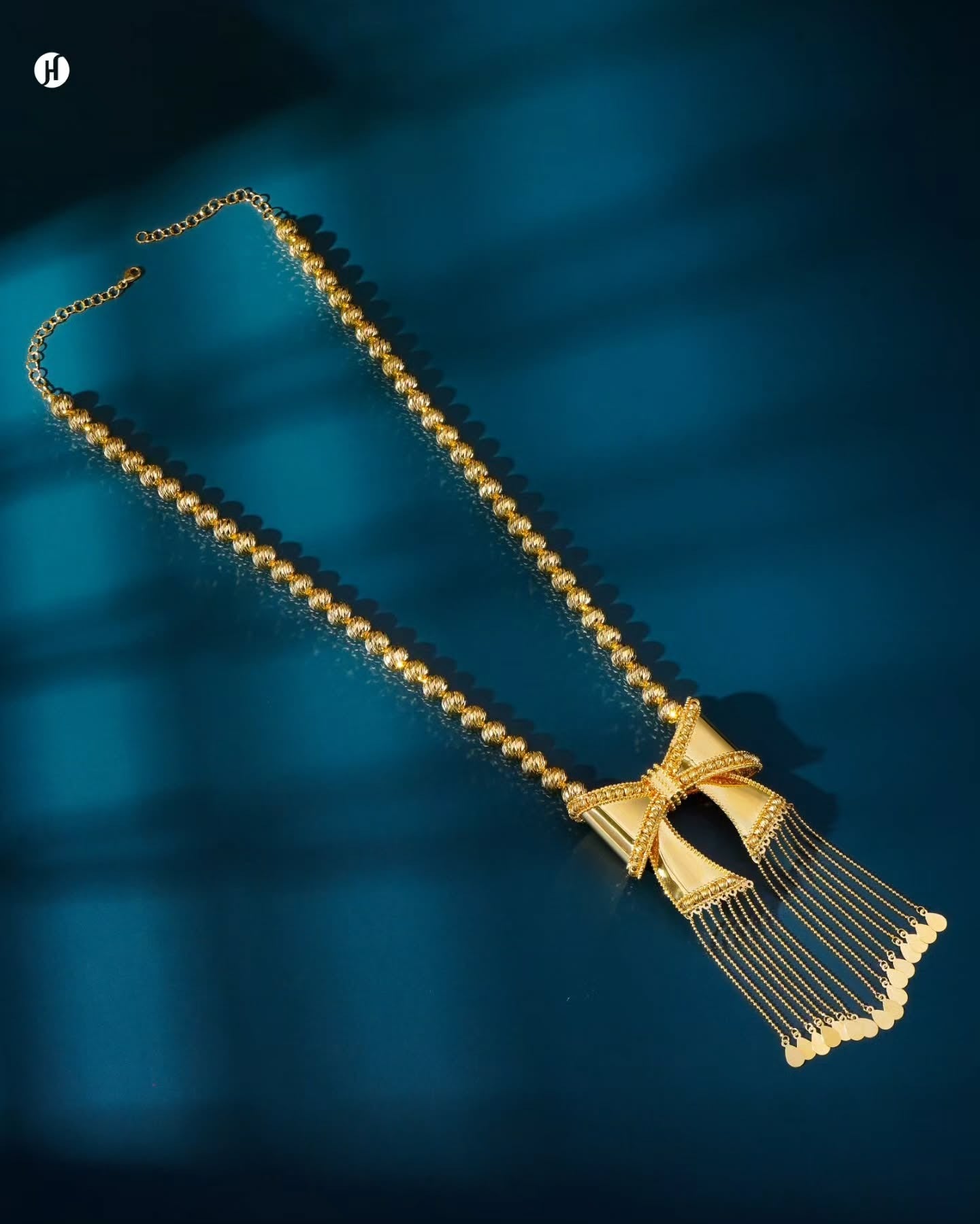 21K yellow gold Bahraini necklace with a textured beaded chain, bow-shaped centerpiece with filigree detailing, and cascading tassel chains tipped with gold teardrop discs.